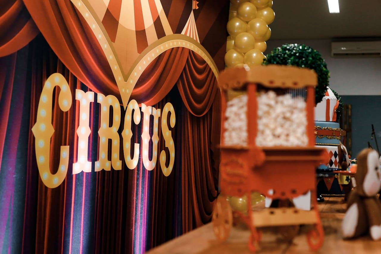 Colorful circus-themed party decorations featuring popcorn cart and balloons indoors.